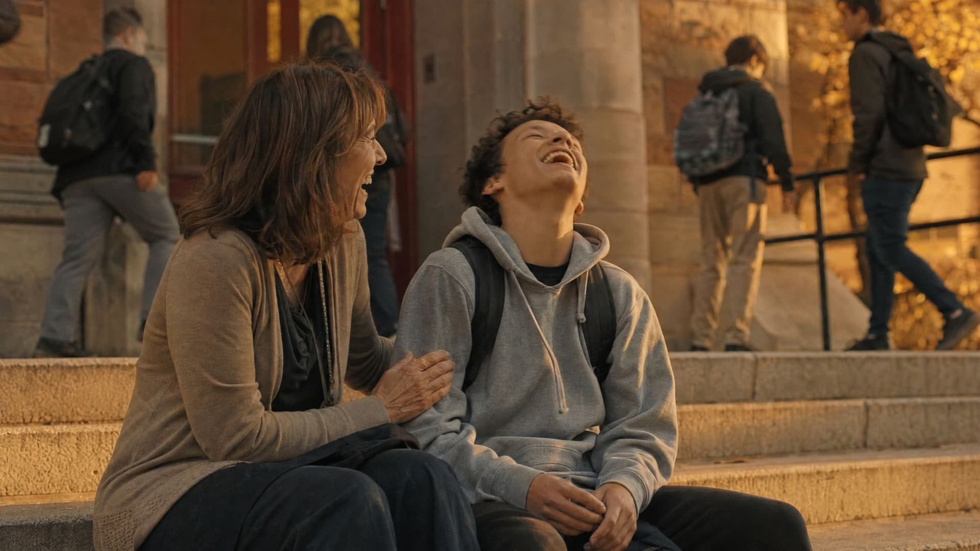 On the school steps, a boy throws his head back laughing with relief as his counselor laughs with him.